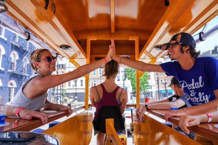 2 people high-fiving on a pedal wagon with Captain driving